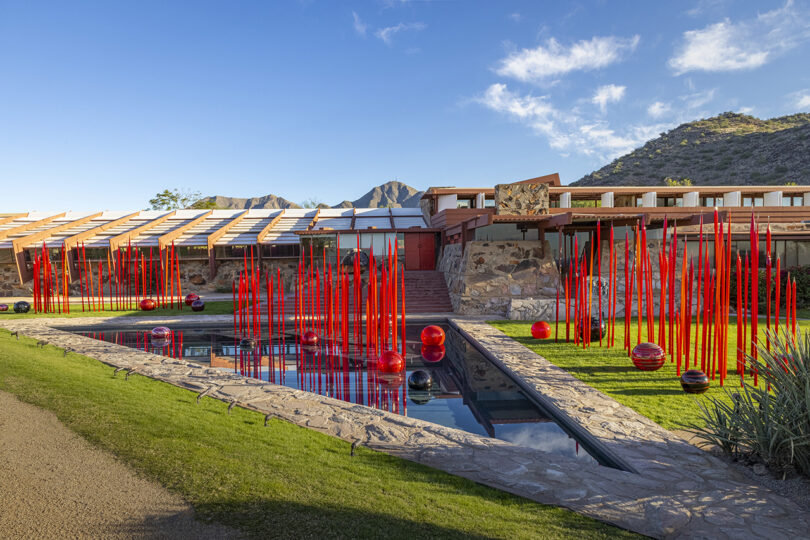modern building with vertical red rods sticking up from the water and grass surrounding it