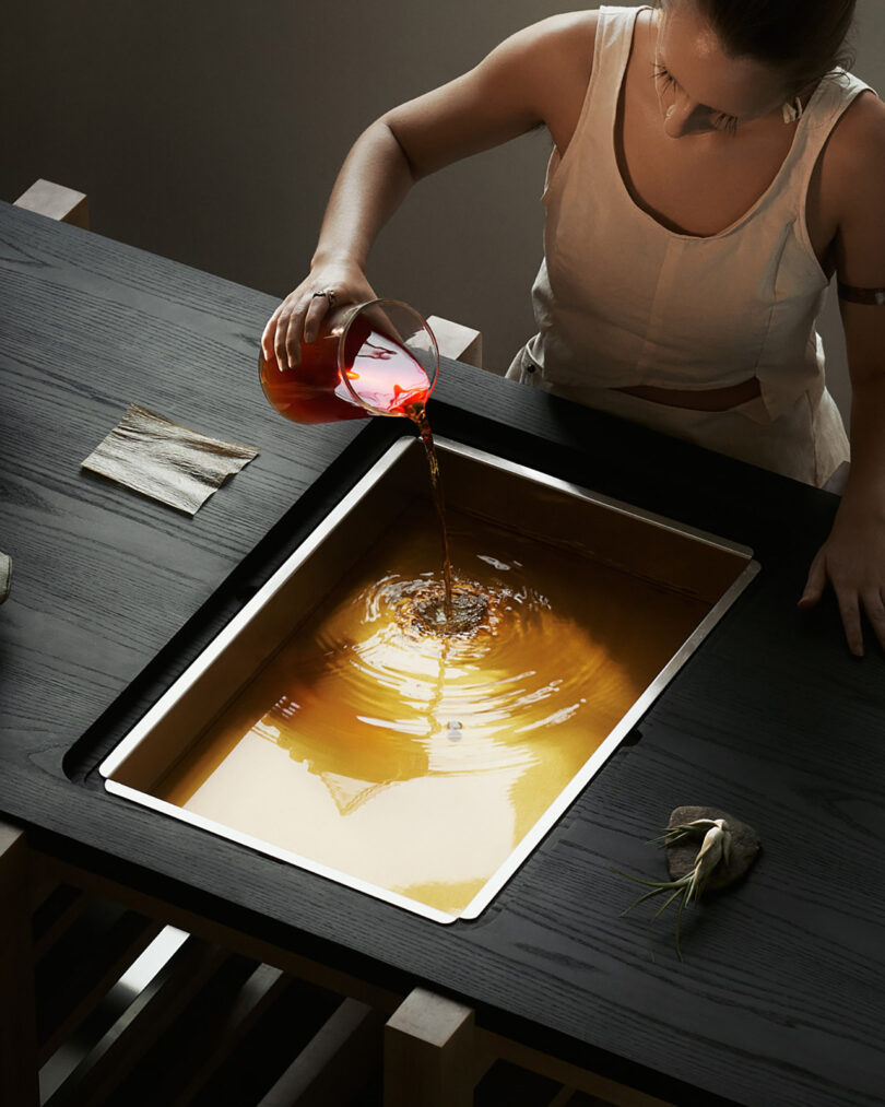 person stands at a table pouring yellow liquid into a large. metal container