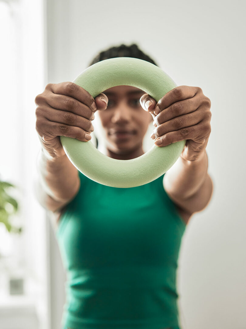 looking towards the upper half of a woman in a green shirt holding a light green ring weight with her face showing through center
