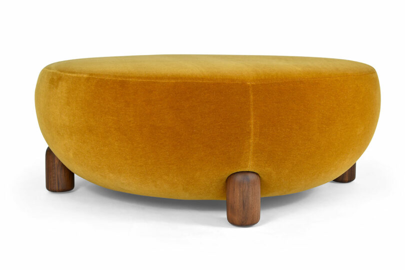 A three-legged ottoman with mustard upholstery.