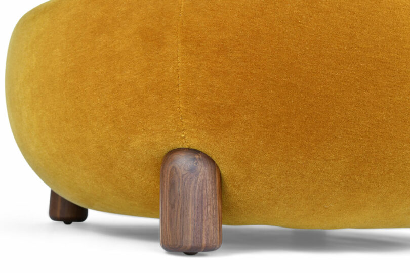 The wooden leg detail of an ottoman with mustard upholstery.