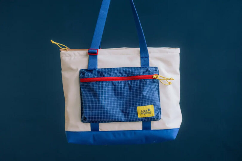 Long Weekend Beacon Tote with extended bright blue shoulder straps staged with a dark blue background behind it