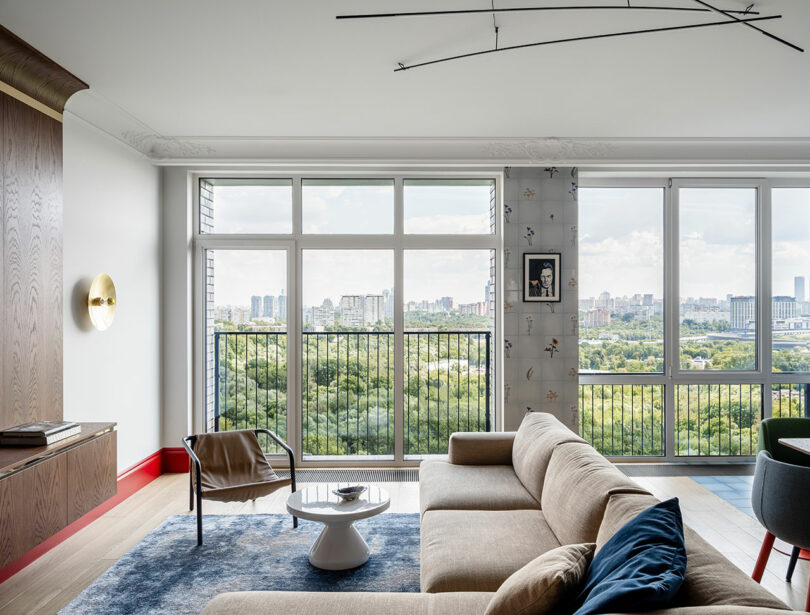 interior view of modern minimalist living room with sectional gray sofa and floor to ceiling windows looking out to city
