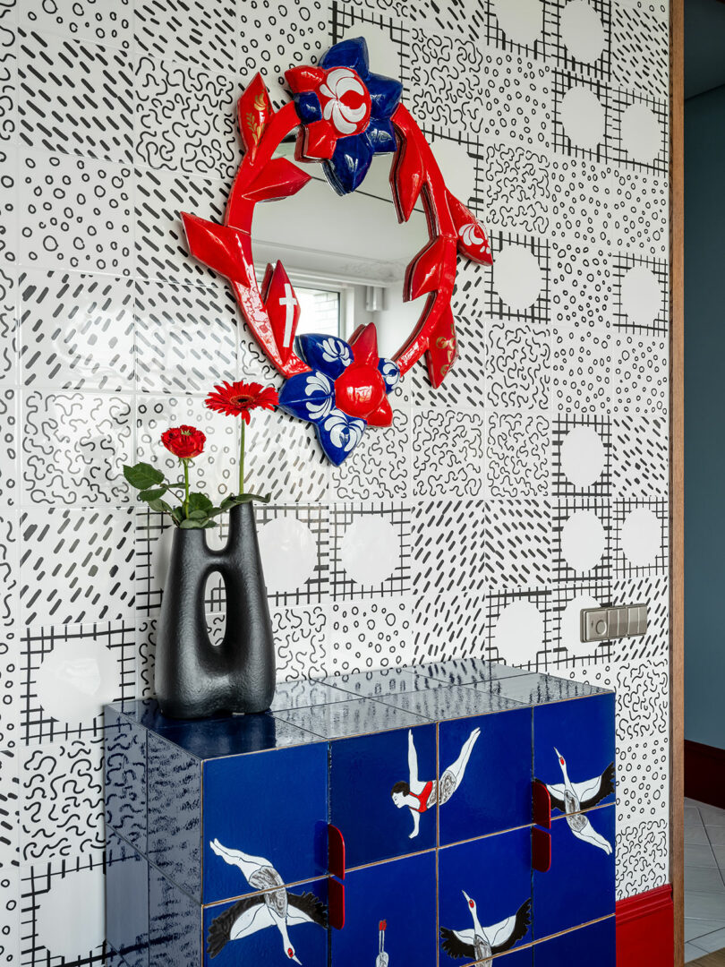 angled closeup of cobalt blue console table with black and white patterned wall tile with quirky red mirror above