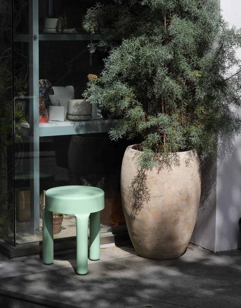 seafoam green stool next to a large outdoor potted plant
