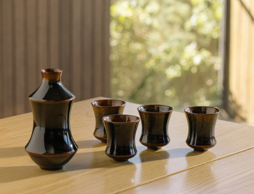 Four ceramic sake cups and vessel with dark speckled and glossy glaze.