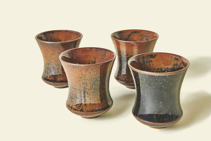 Four ceramic sake cups with dark speckled and glossy glaze.