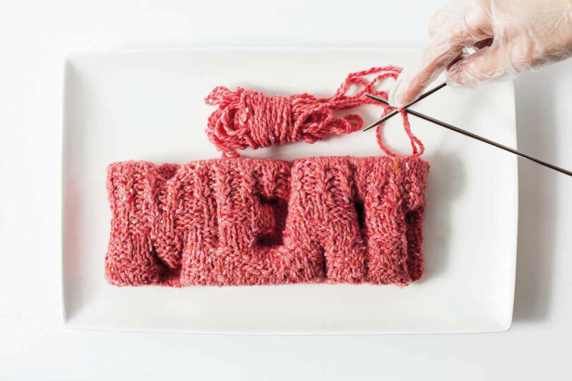 Yarn made to look like ground beef being knitted, spelling out MEAT
