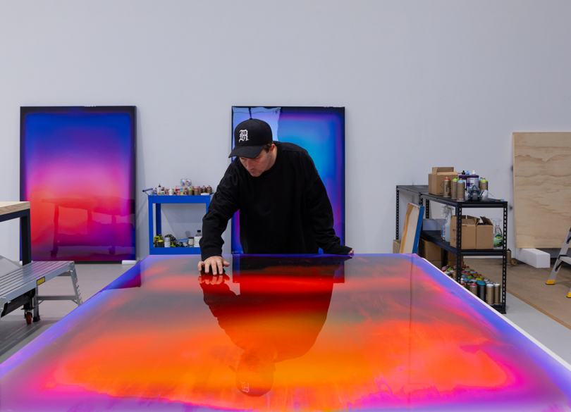 light-skinned man wearing a black shirt and baseball hat works on a large-scale piece of resin art