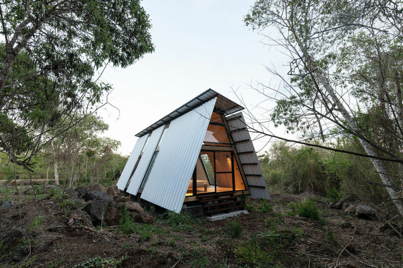 angled exterior shot of three paneled A-frame cabin in woods