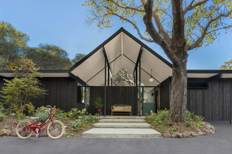 Front and center exterior view of black Eichler home with large vestibule area with white ceiling