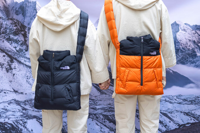 Two people in white snow suits facing away from camera each with a puffer crossbody bag