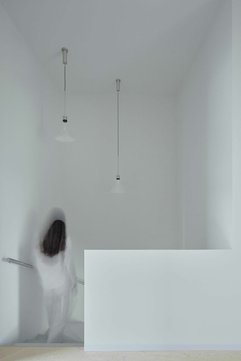 interior view of upstairs in all-white space as blurry woman walks down stairs