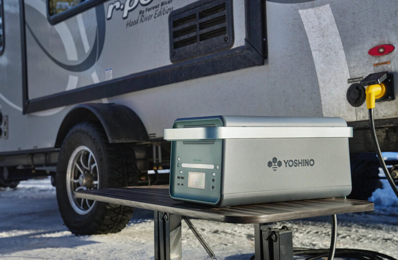 Yoshino portable solid-state battery station set on an outdoor table near a recreational trailer/vehicle.