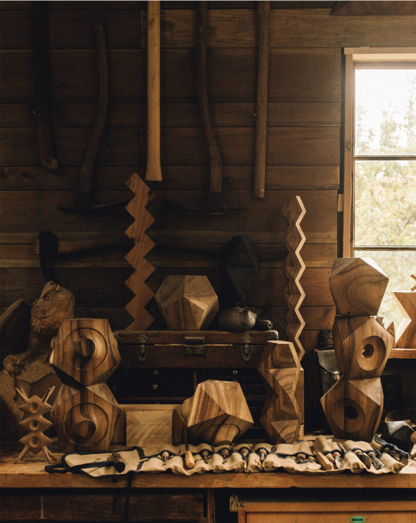 Numerous wood carved geometric sculptures of artist Aleph Geddis inside his wood carving shed on Orca Island, with several of his tools laid out on display across an unrolled fabric carrying case.