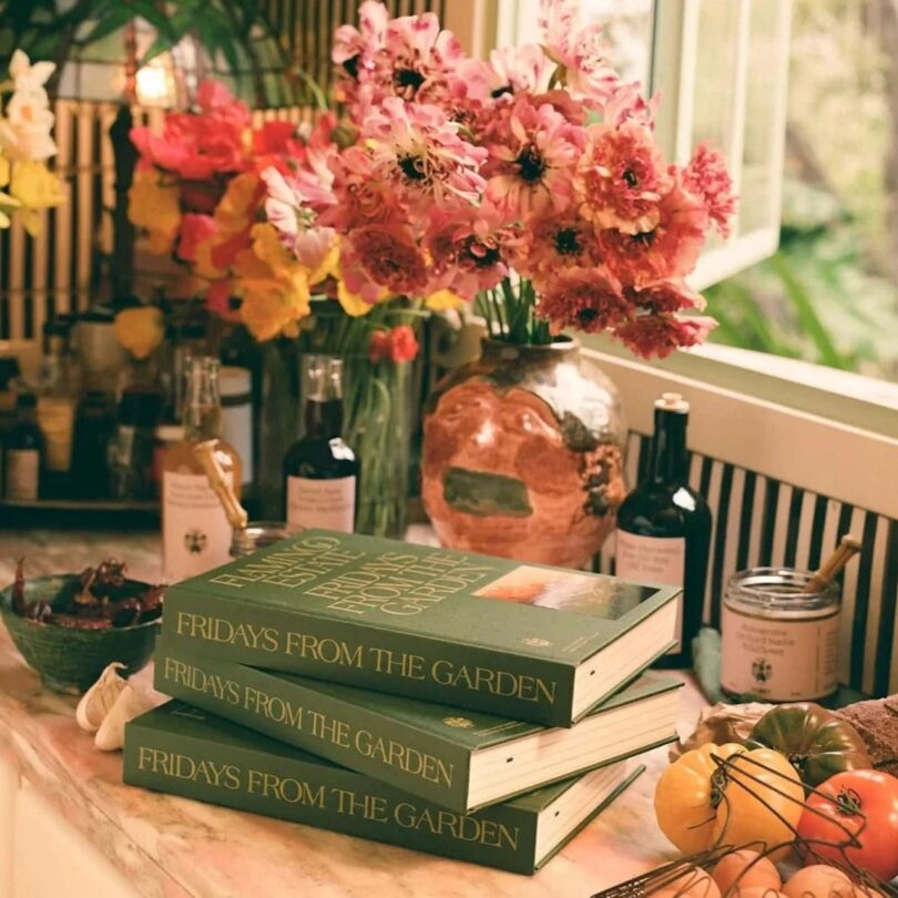 cookbooks stacked on table next to produce and flowers