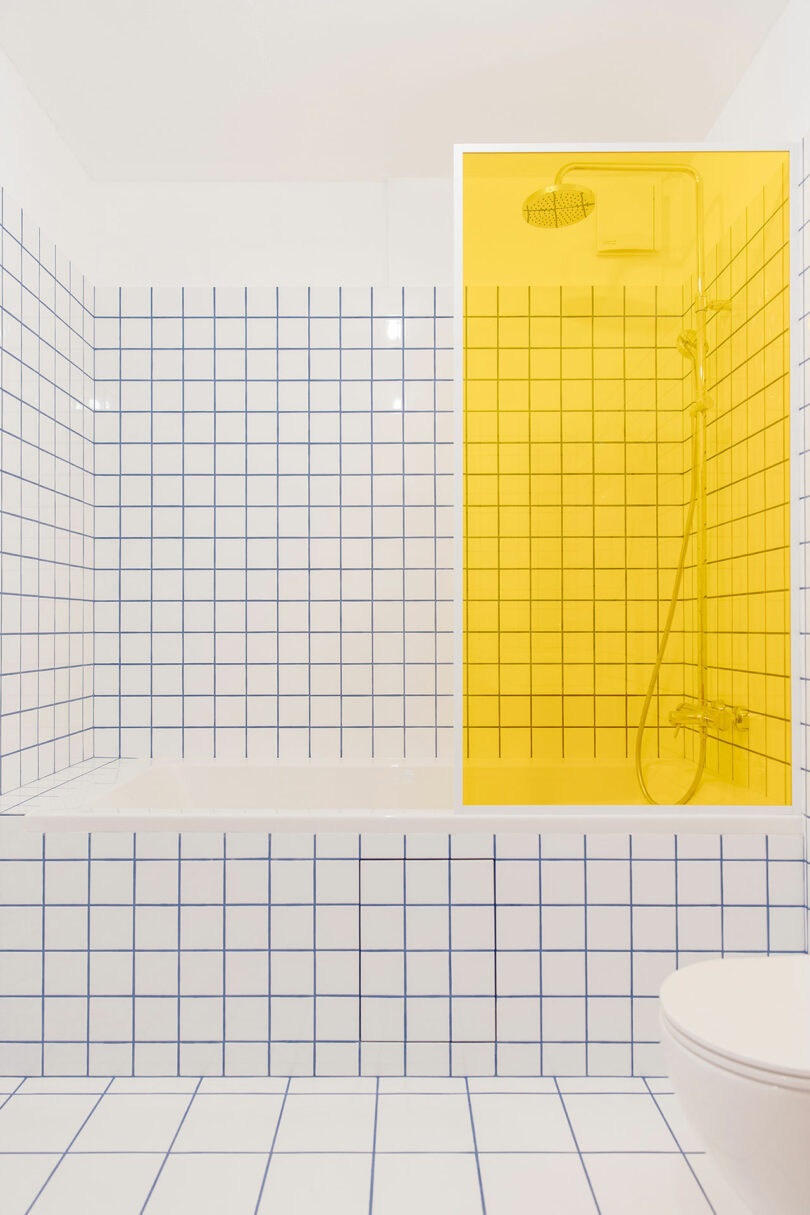 view in modern bathroom with white grid tile and blue grout with yellow glass partition
