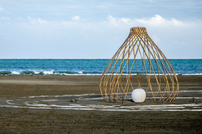 wood cage-like art installation on a beach