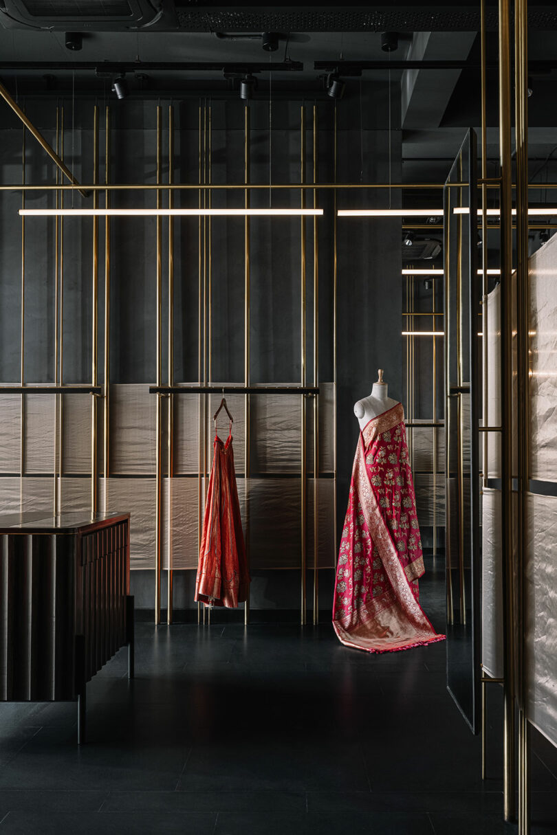 Vertical golden rods from which shelves are built and garments hang. Two dresses displayed.