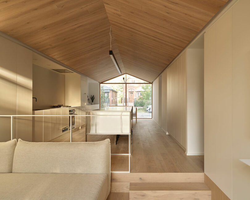 long interior view of open living space in modern house with light wood gabled ceiling and neutral furnishings