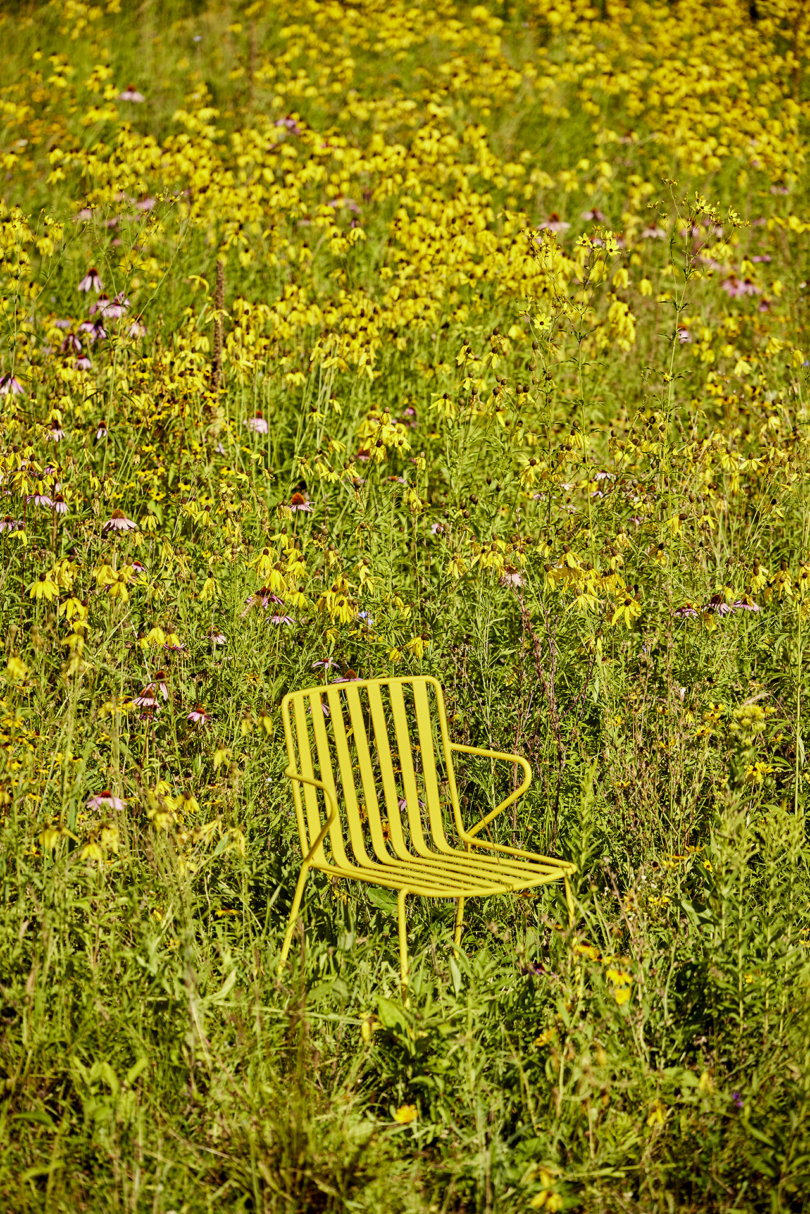 yellow slatted metal outdoor chair in a field of grass and flowers