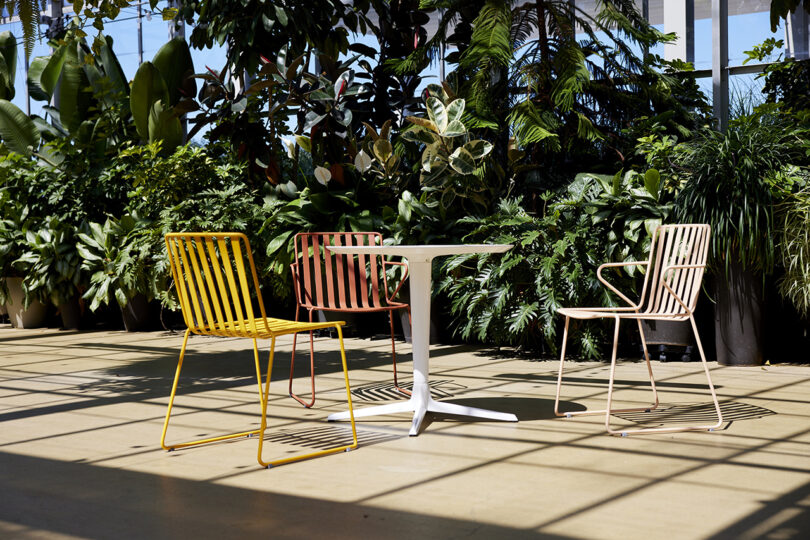 three colorful slatted metal outdoor chairs surrounding a white cafe table