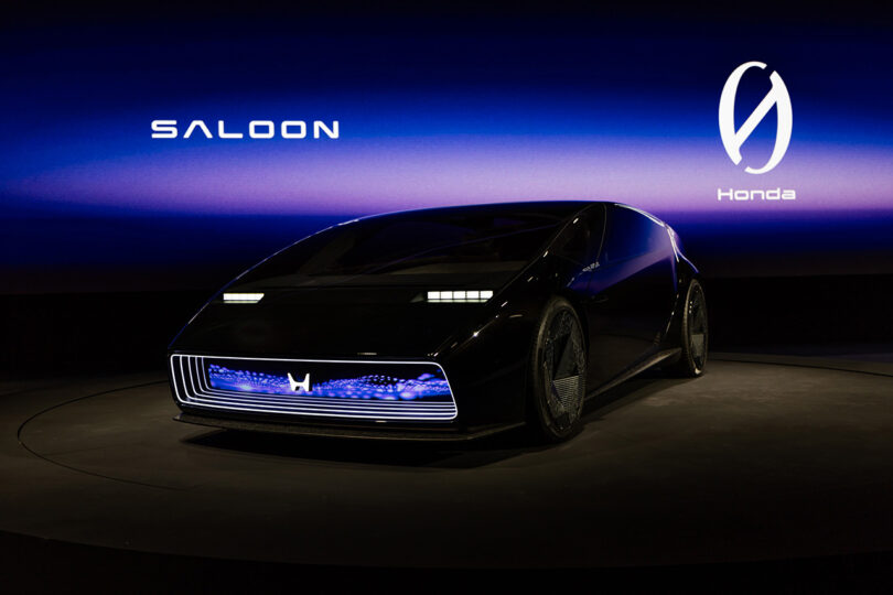 Honda's new Saloon concept, one of two new Zero Series vehicles unveiled on stage at CES 2024, with large wide screen showcasing the new Zero Series logo. Car's front lights are illuminated.