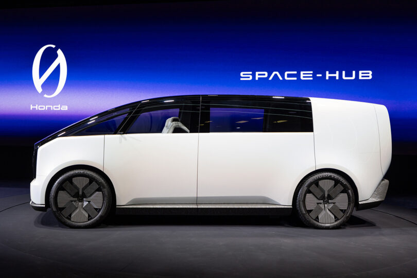 Side profile view of Honda's new Space-Hub minivan concept, one of two new Zero Series vehicles unveiled on stage at CES 2024, with large wide screen showcasing the new Zero Series logo in background.