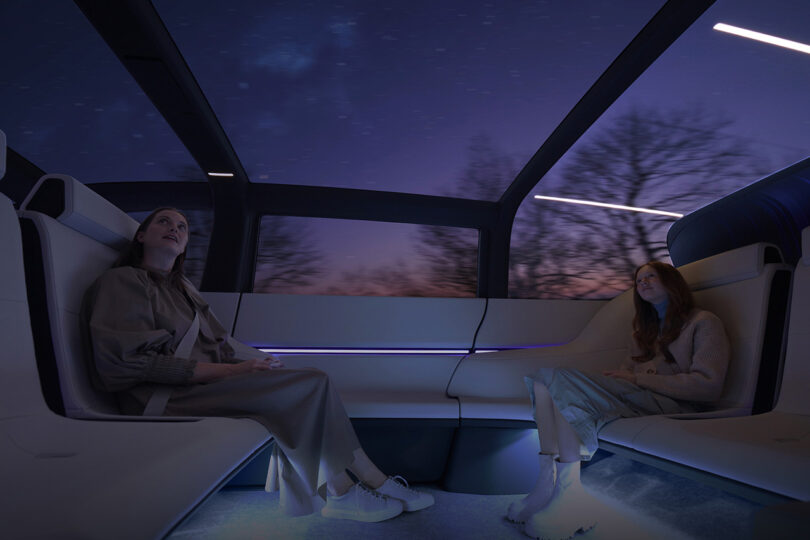 Interior passenger seating of Honda's Space-Hub futuristic EV minivan, with two women staring overhead through the van's panoramic moonroof.