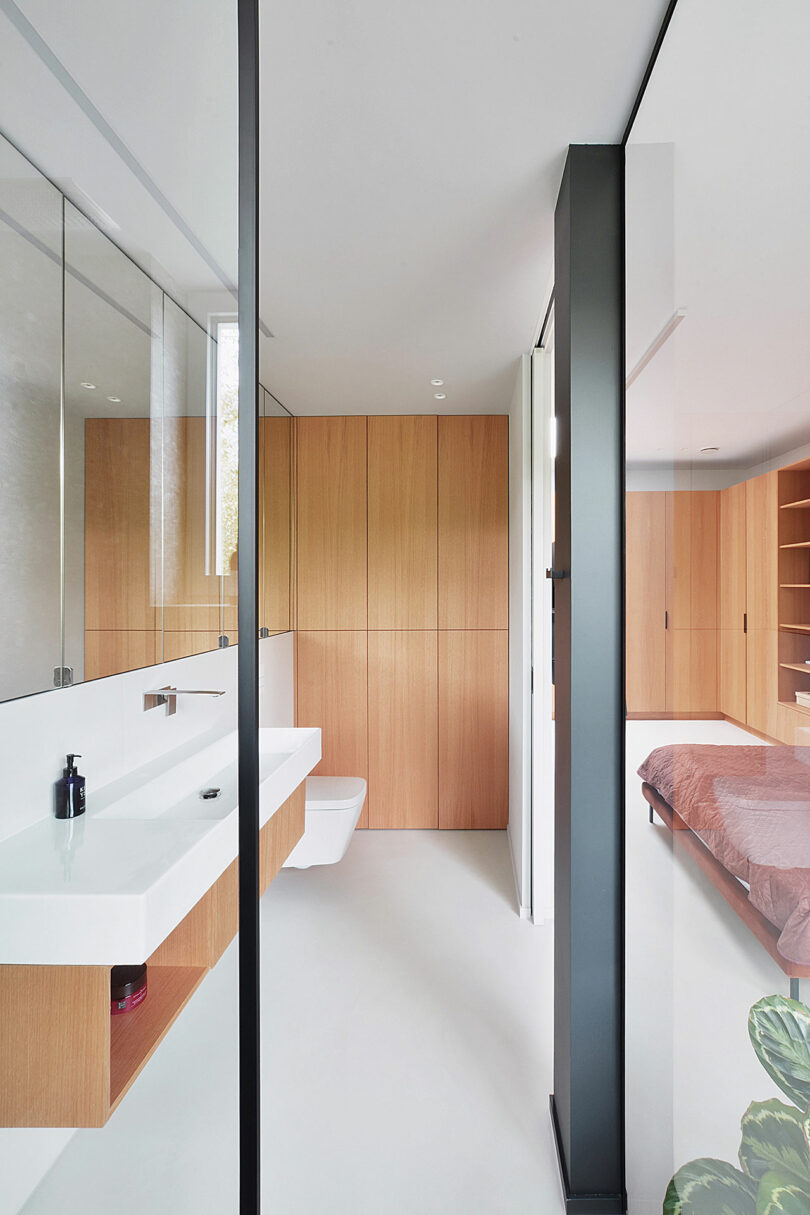 view into modern open bathroom with glass walls, wood cabinets, and white floating console