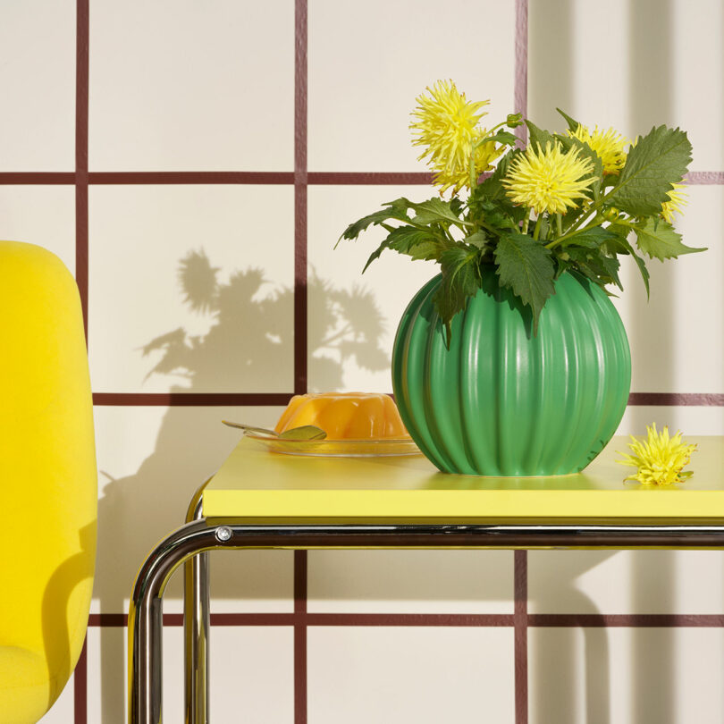 view of yellow and chrome cart holding bulbous green vase with yellow flowers