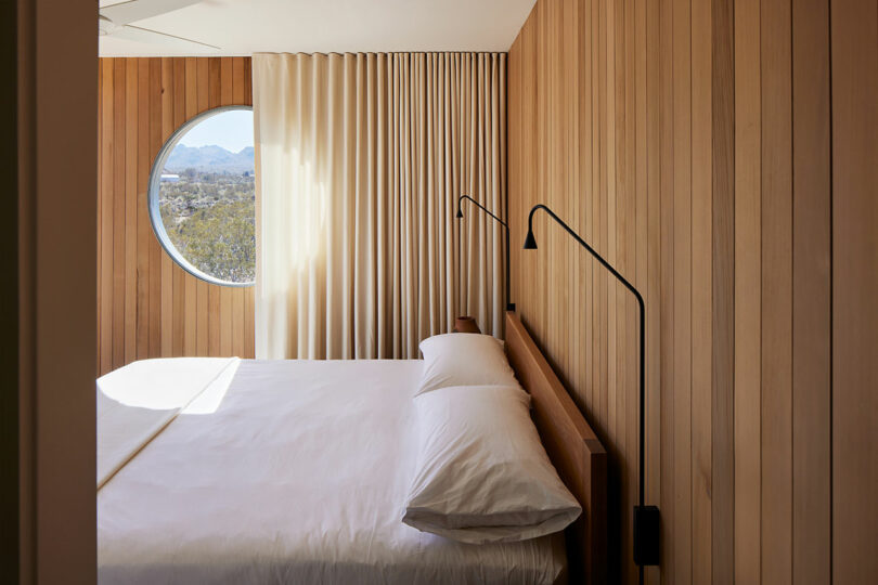 partial view of modern minimalists bedroom with simple white bedding and circular window on far wall
