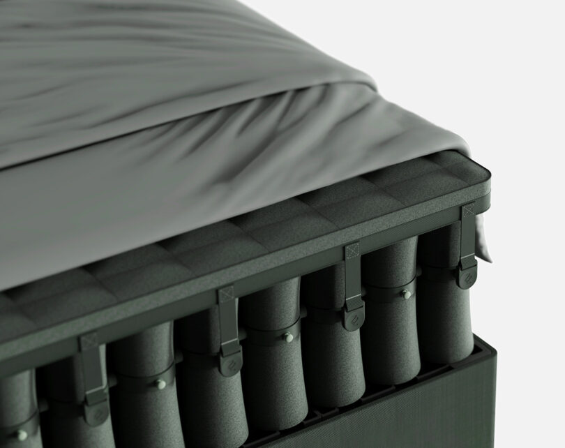 Close up of green MAZZU modular mattress made up of a system of fabric wrapped hourglass shaped inner springs positioned in a stacked column layout, with sheets placed over it.