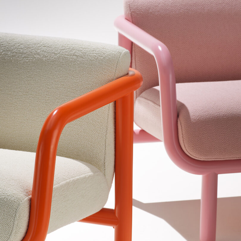 Two Percy lounge chairs side by side in off-white upholstery and bright orange tube frame, alongside one in pink frame and upholstery. 