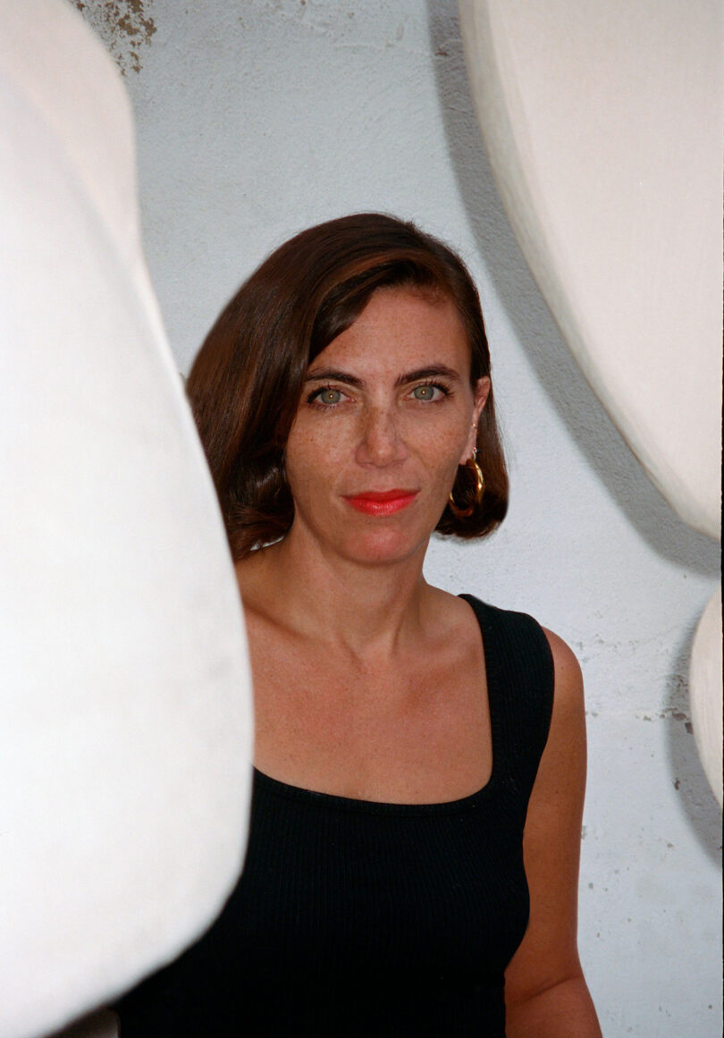 light-skinned, dark haired woman wearing red lipstick and a sleeveless black shirt