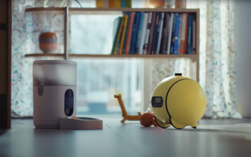 Yellow 3-wheel Samsung AI robot Ballie sending signal to network compatible pet food dispenser