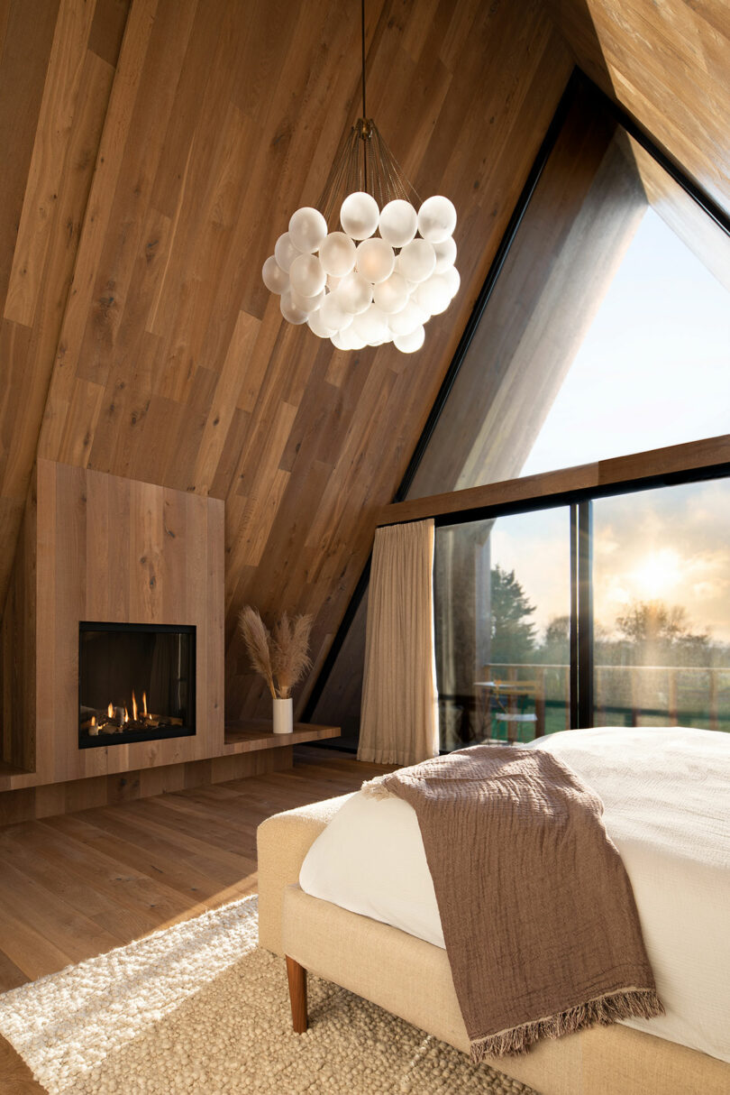 angled interior view of large modern bedroom under steep pitched wood ceiling with ball chandelier