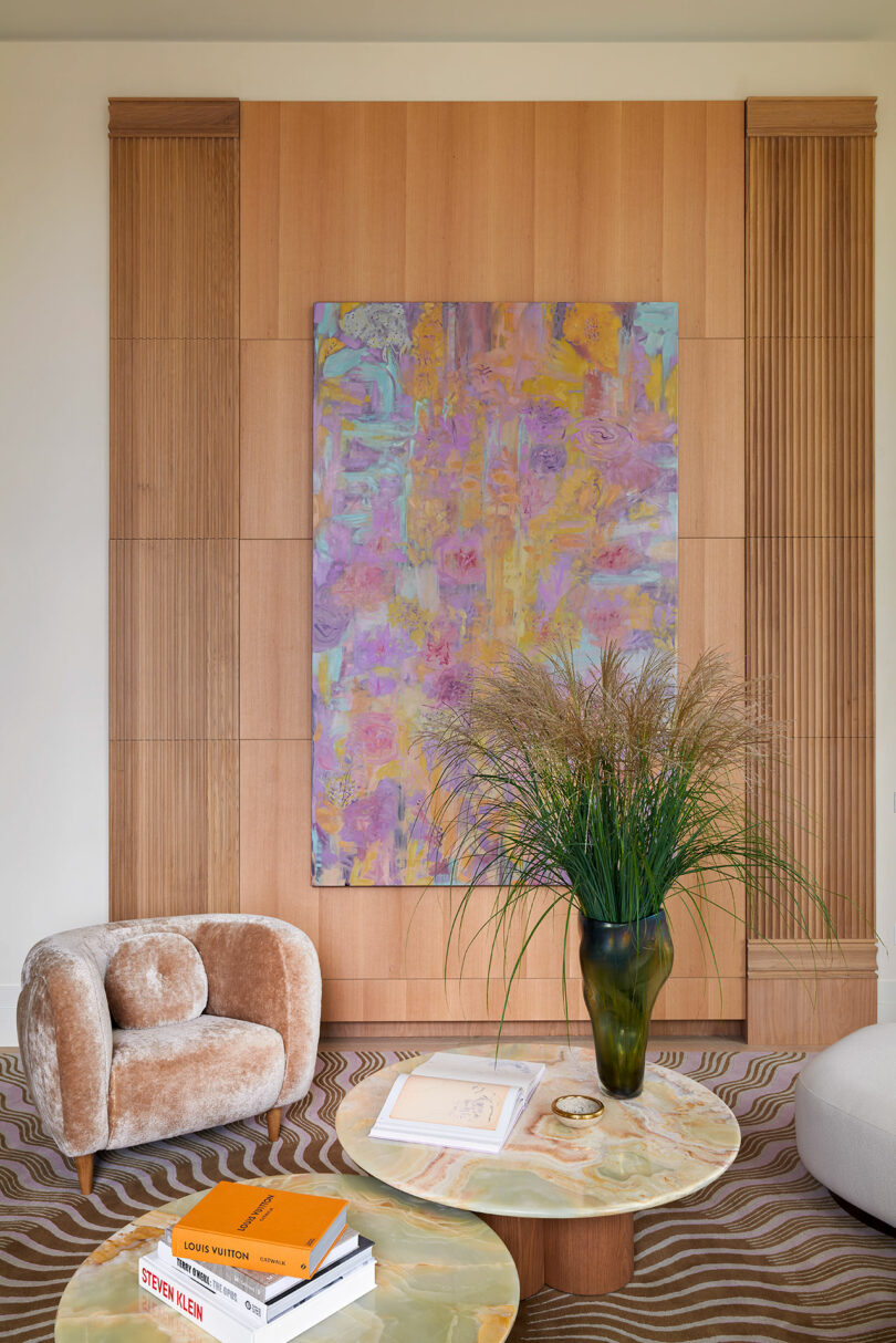 interior shot of partial modern living room with pink upholstered chair behind coffee tables with a large piece of modern art hanging on wall behind
