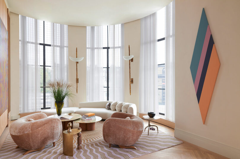 modern living room with curved windows, featuring a curved white sofa and two pink upholstered chairs
