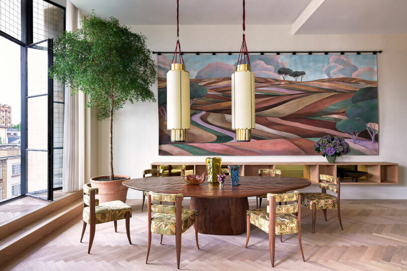 modern dining room with oval wood table and patterned wood chairs surrounding with large abstracted landscape painting hanging on wall behind