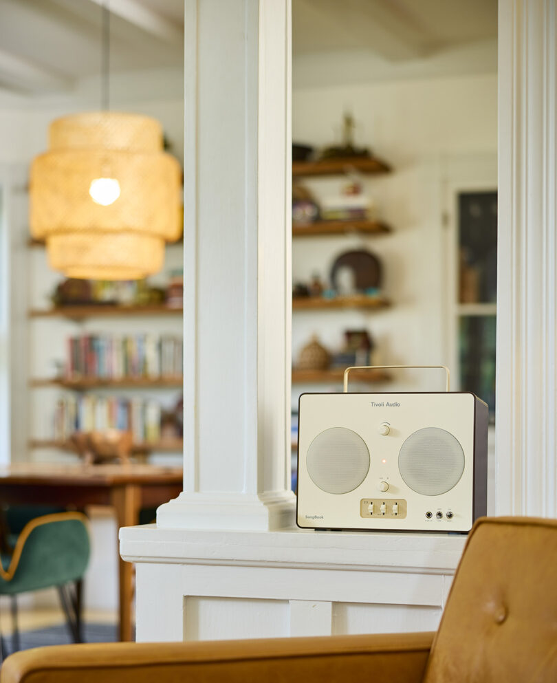 Tivoli SoundBook in Cream and Brown in living room environment staged near a midcentury armchair in the foreground and hanging pendant light, shelving in the background
