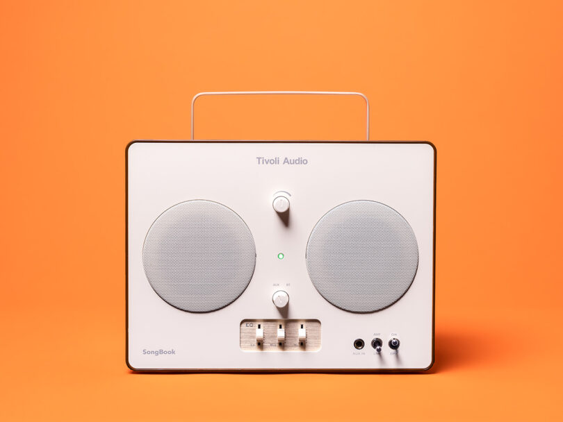 Tivoli Audio SongBook wireless speaker power pinch grip group against an orangish background.