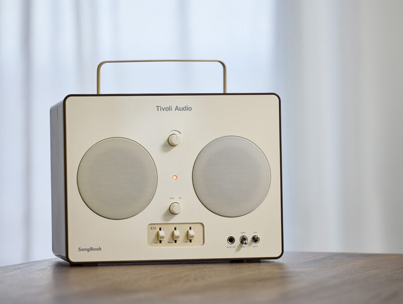 Tivoli Audio SongBook wireless speaker radio with handle on wood circular table.