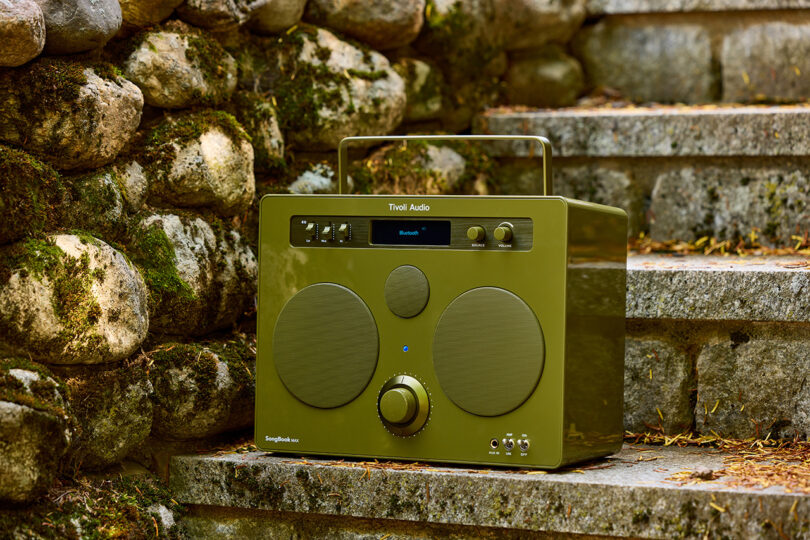 Tivoli Audio SongBook MAX wireless speaker radio in glossy green set on outdoor stone steps.