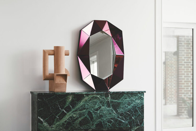 A multifaceted mirror and sub on a marble fireplace mantel.