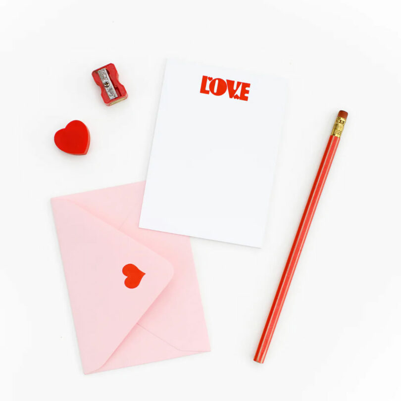 A Valentine's Day Stationary Set pinch achromatic statement card, pinkish envelope, and reddish pencil, eraser, and sharpener.