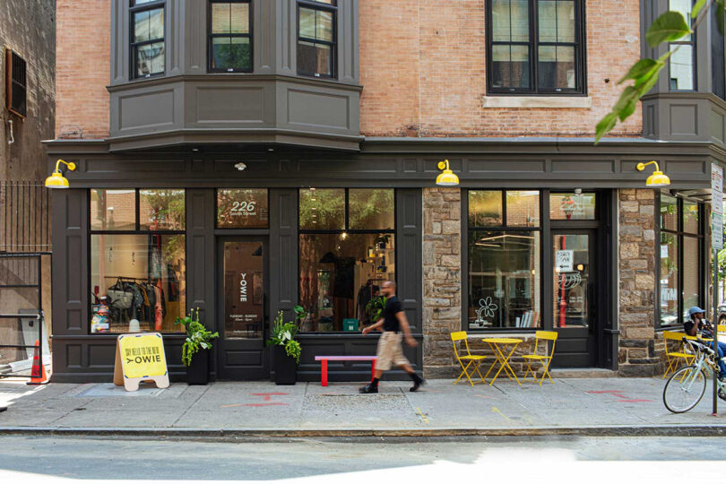 Exterior of the YOWIE hotel in Philadelphia with man in shorts walking by. Yellow signage out front pointing toward hotel entrance, with yellow cafe seating nearby.
