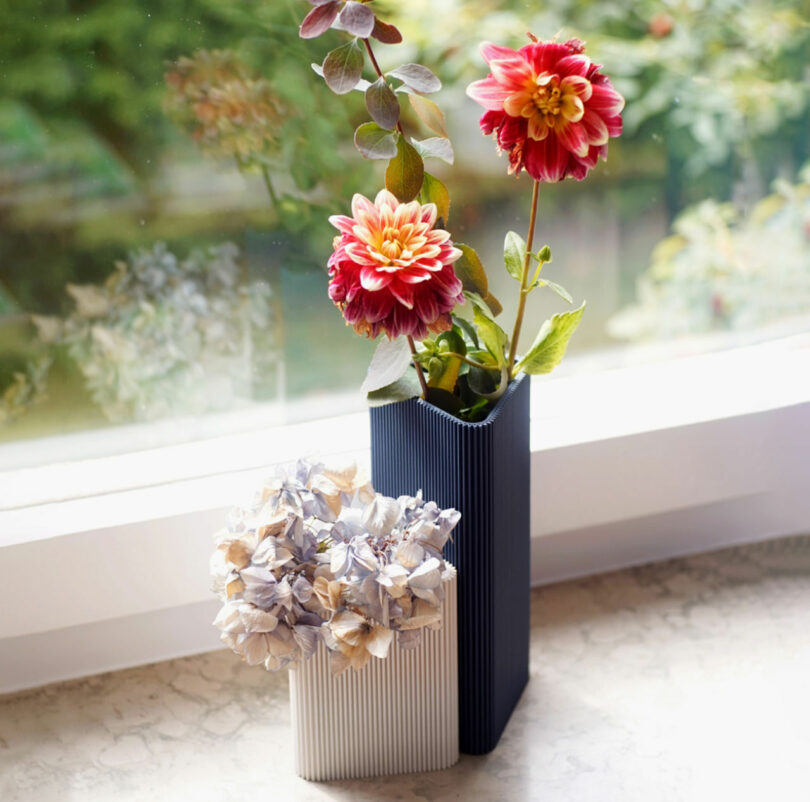 two triangle vases with flowers in them next to a window