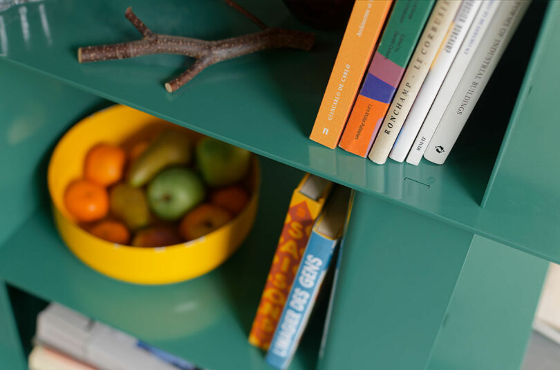 green multi-level metal shelf with books and fruit on it