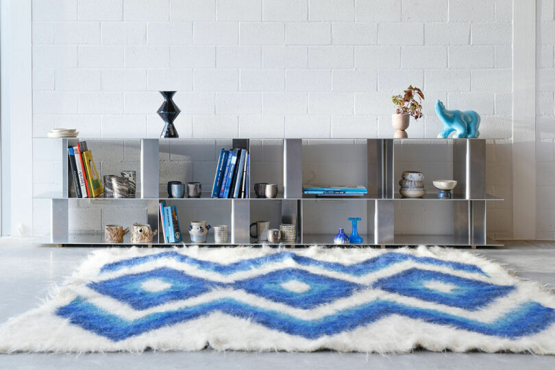 aluminum modular shelving system with books and objects on it next to a blue and white rug